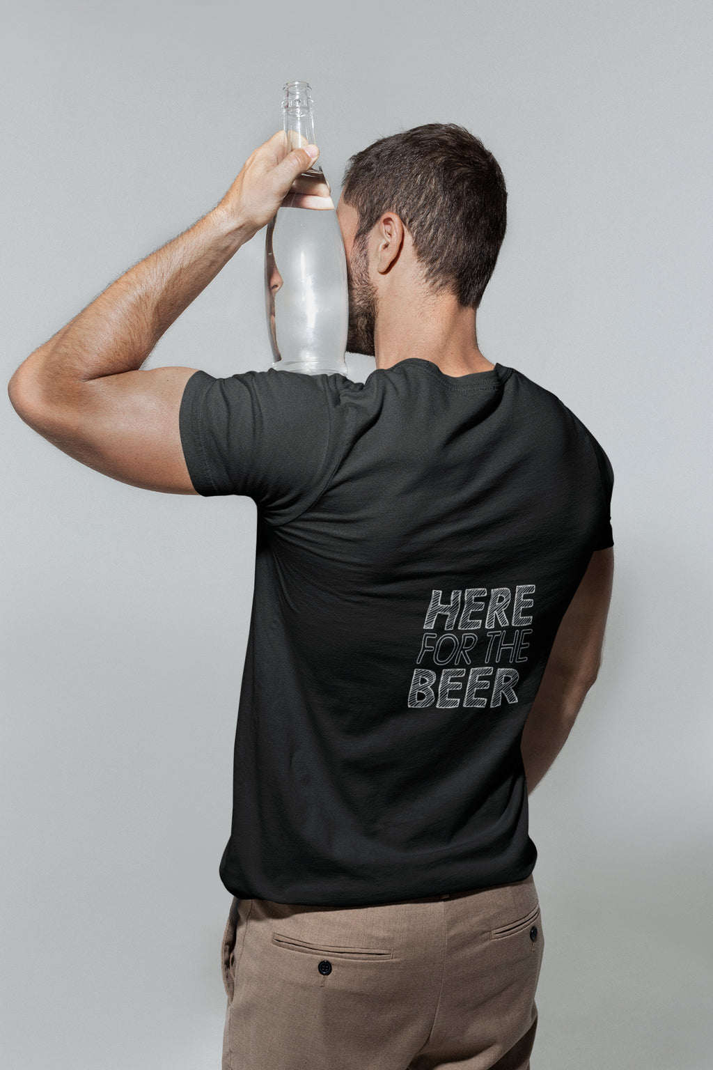 Man wearing a black t-shirt with 'Here for the Beer' text, holding a bottle against a plain background
