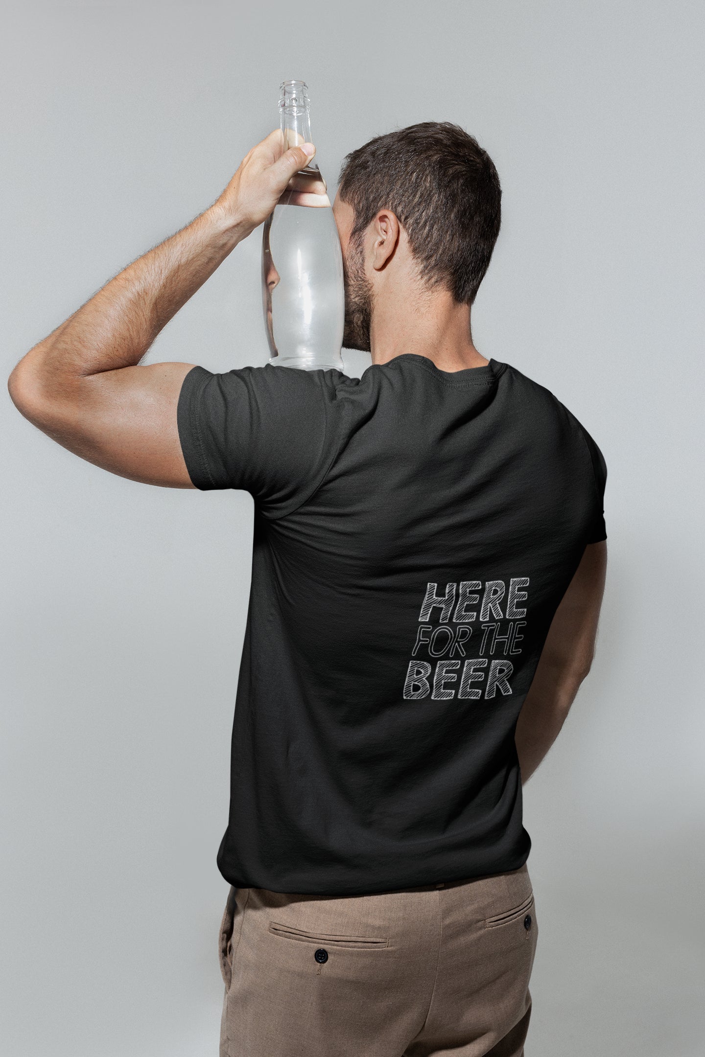 Man wearing a black t-shirt with 'Here for the Beer' text, holding a bottle against a plain background